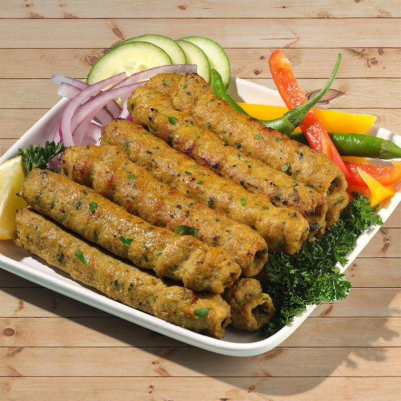 10 Kaiser Charcoal Chicken Kababs are arranged in a stack 5 on 5 on a plate with sliced, cucumber, red onion, peppers and leafy greens.