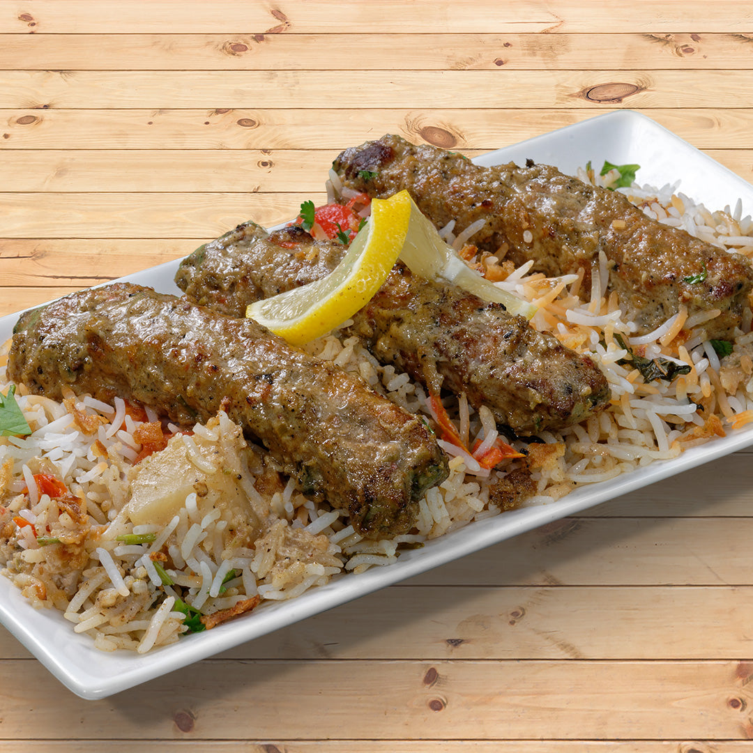 Chicken kababs rest on a bed of biryani rice, they are garnished with a strip of lemon