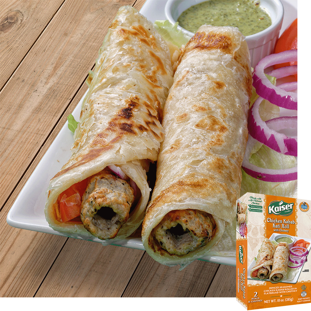 2 kati rolls made with chicken kebabs and wrapped in paratha are on a plate with a bowl of green chutney sitting behind them some rings of red onion are next to the rolls. A box of Kaiser Chicken kebab Kati Rolls is in the bottom right corner.
