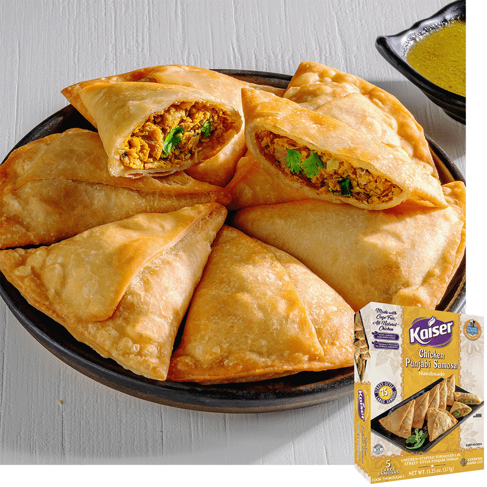 A black plate with 7 chicken punjabi samosas on it arranged into a ring with one samosa on top cut open exposing a a minced chicken stuffing and visible cilantro. A package of Kaiser Chicken Punjabi Samosas is overlaid in the bottom right corner.