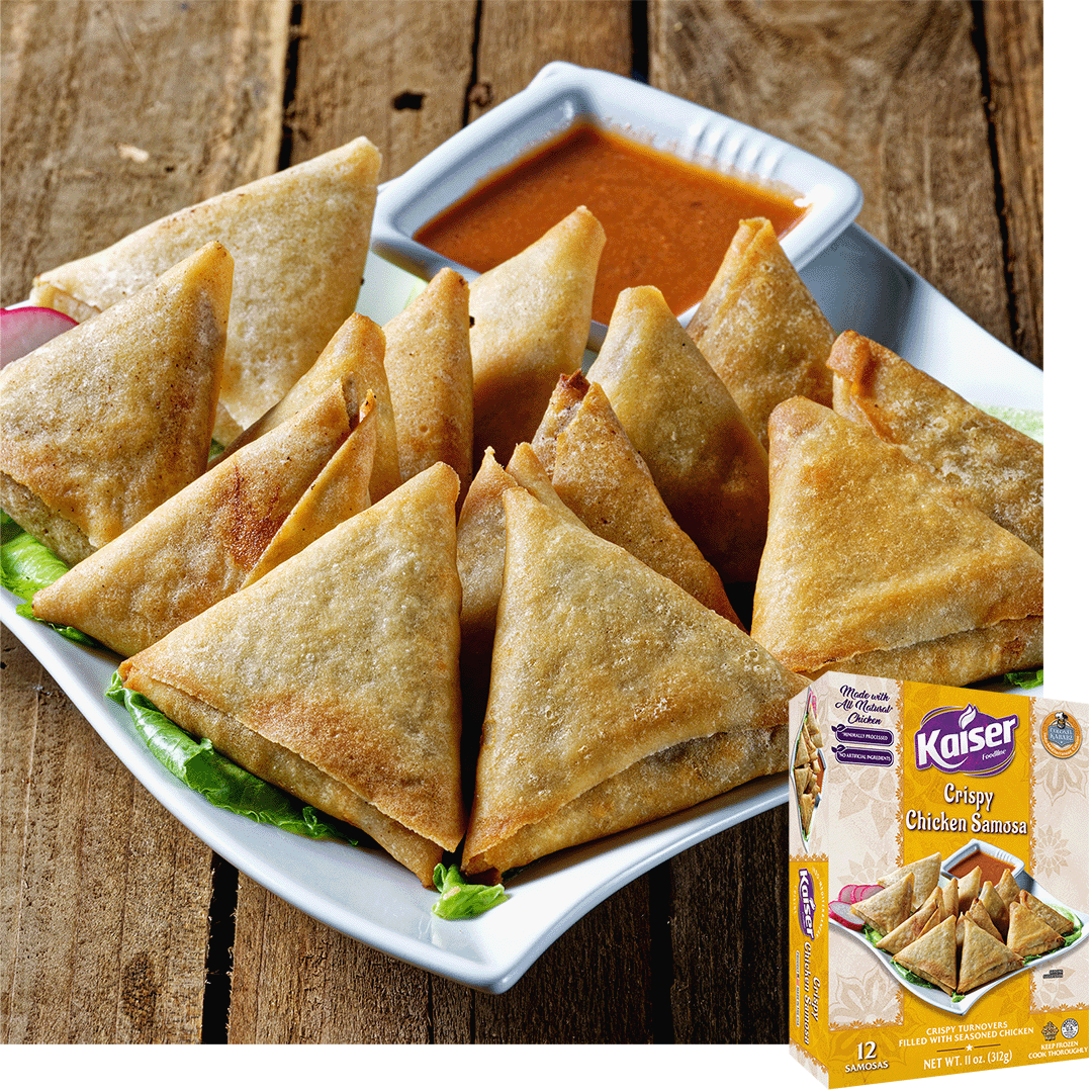 A white plate with crispy chicken samosas resting on a bed of lettuce. The samosas are garnished with a slice of radish and served with a bowl of reddish orange sauce, in the bottom right hand corner is an image of the product packaging