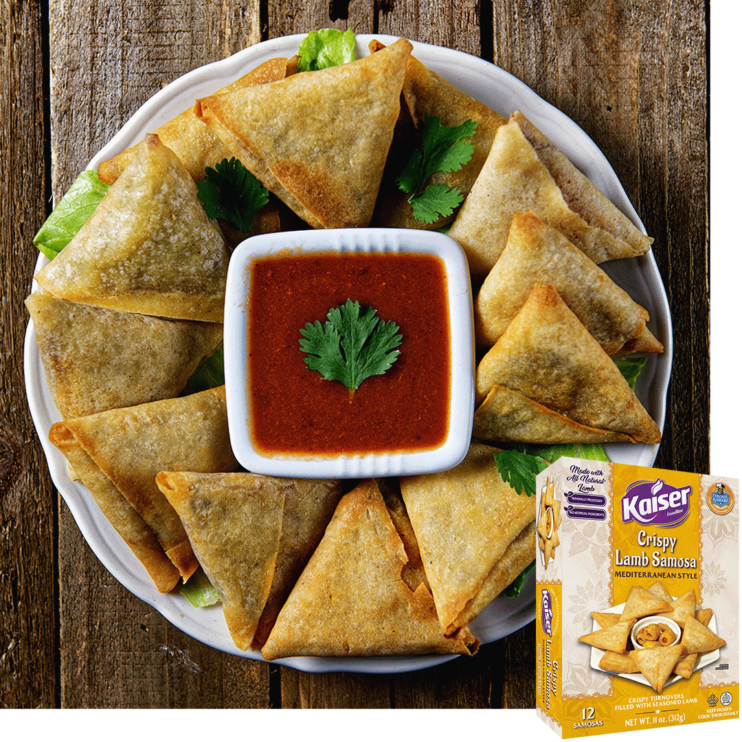 crispy lamb samosas arranged on a white plate, in the center is a square bowl with a red sauce. In the center of the sauce is a single leaf of cilantro, the rest of the plate is garnished with leaves of cilantro. The plate rests on a wooden background, in the bottom right corner is an image of the product package