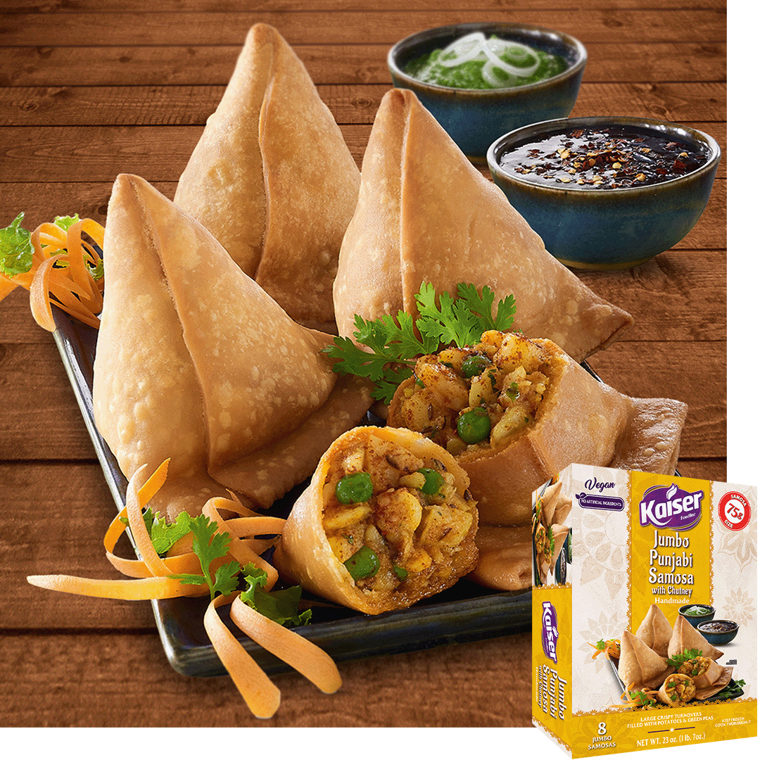 Jumbo punjabi samosas sit on a black plate. One samosa is cut in half to reveal the filling. The plate is garnished with strips of carrot and pieces of cilantro, in the background is a green sauce with onion strips and black chili sauce. In the bottom right hand corner is an image of the product package