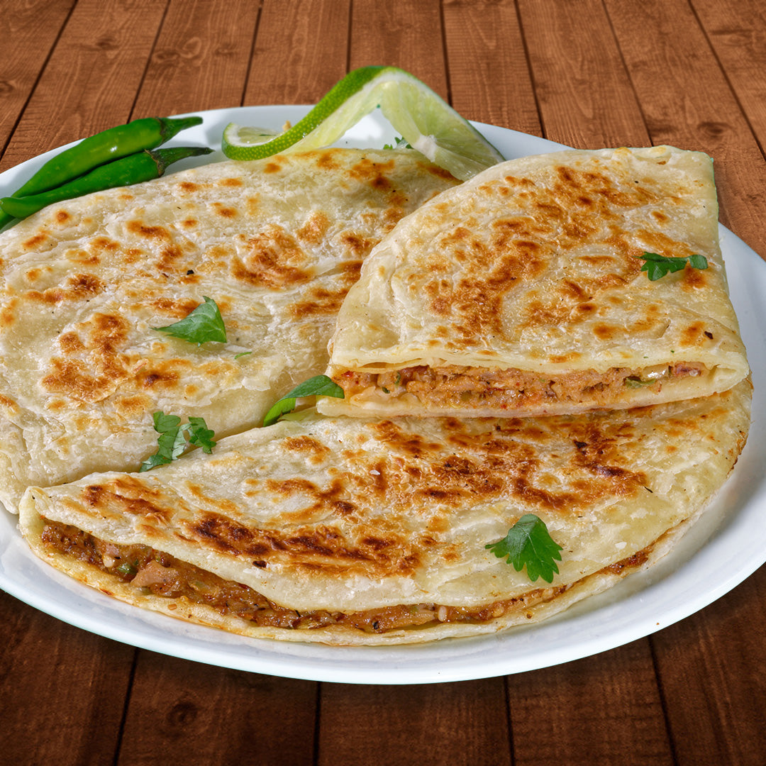 2 Keema paratha are on a plate half of one is stiting one top. Inside the paratha is a ground lamb and hcicken mix with small pieces of vegetables. There are a few pieces of cilantro spread around them.