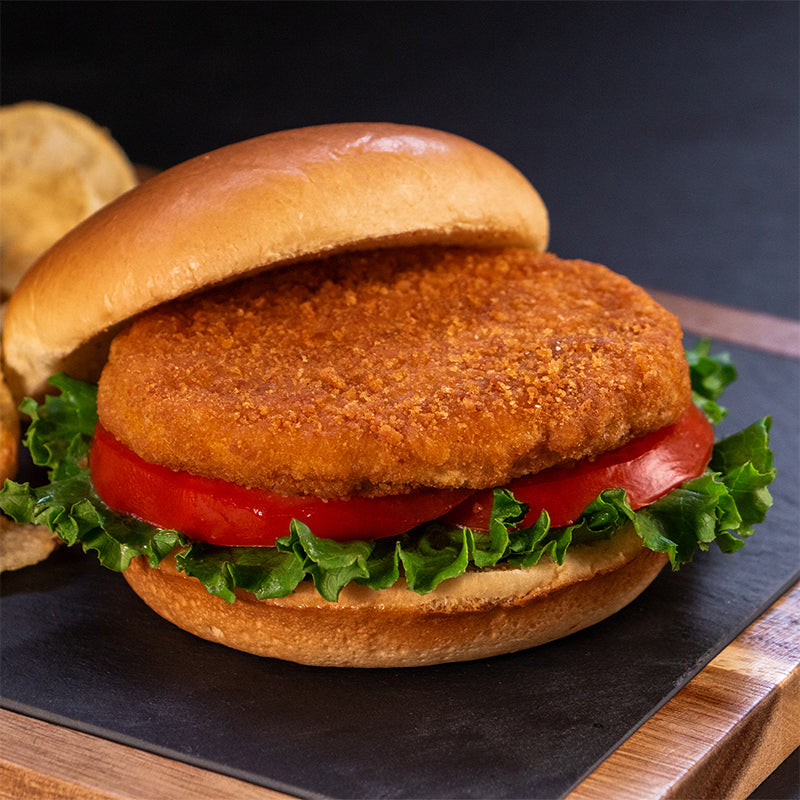 A Halal chicken patty on a bun with tomato and lettuce on a black cutting board.