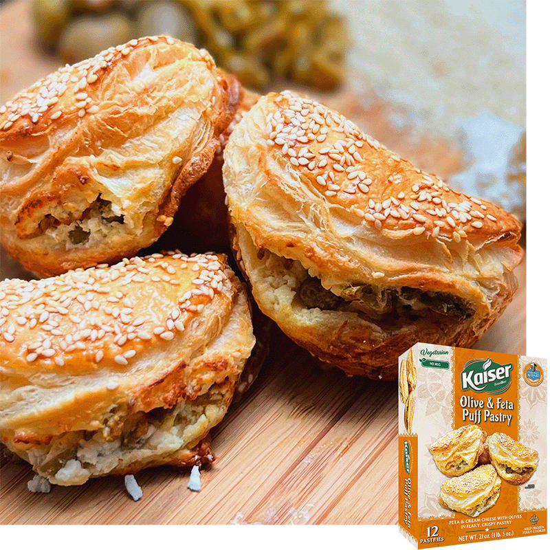 3 Kaier Olive and Feta Puff pastries are laying against each other. They have visible sesame seeds on top and feta crumbles and olive pieces coming from the opening in the flaky layers. A package of olive and feta puff pastry is overlaid in the bottom right corner.