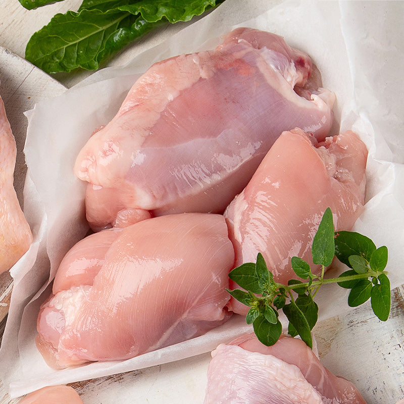 Raw chicken thighs resting on parchment paper, beside them rest a garnish of herbs
