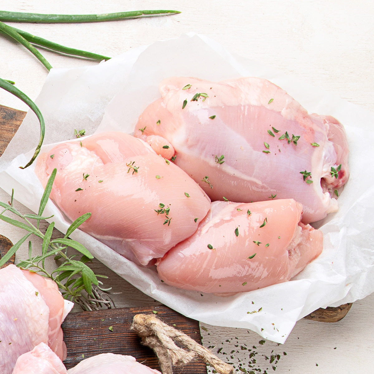 Raw chicken thighs sitting on parchment paper. The chicken is garnished with herbs